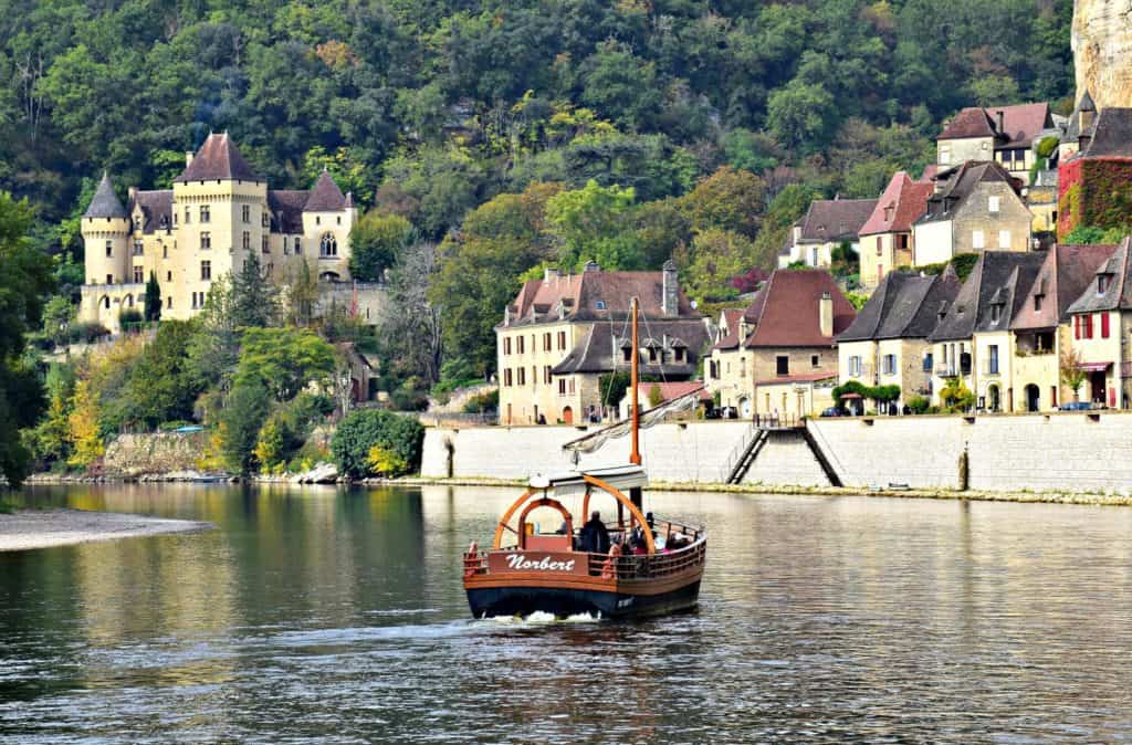 A boat on the Dordogne river in front of a castle and medieval houses in La Roque Gageac