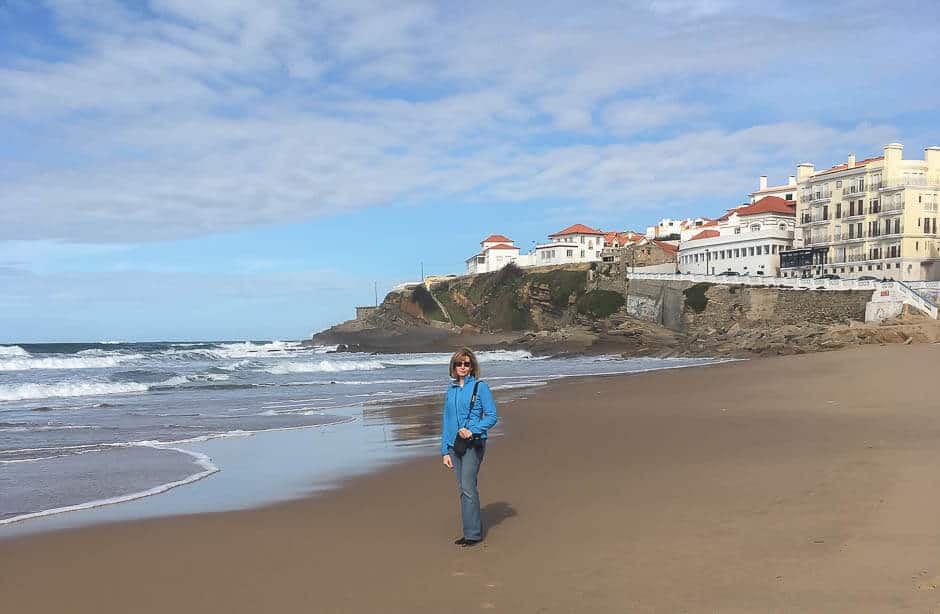 Woman standing on a beach with a town on a cliff in the background