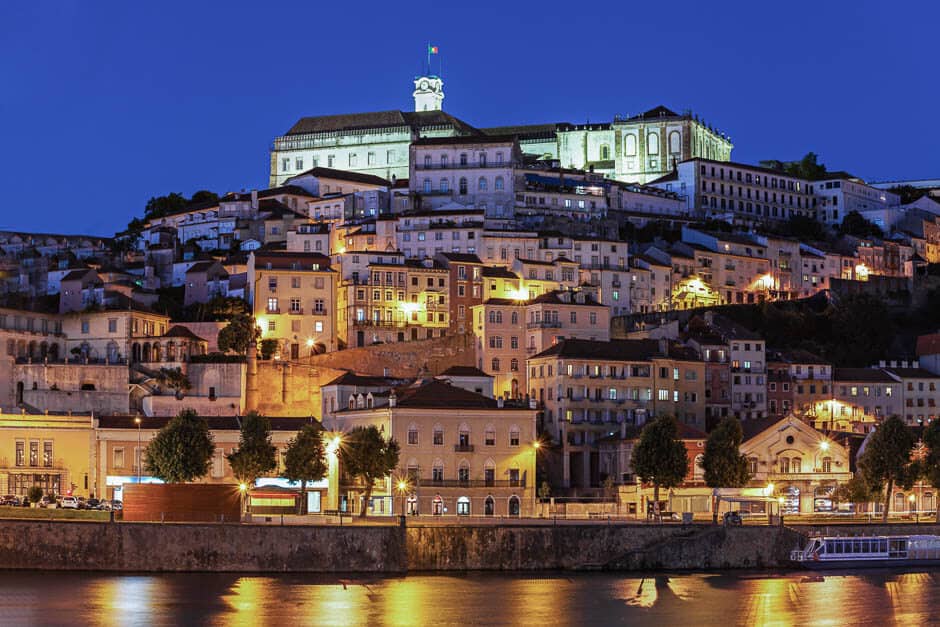 Medieval houses rising from a river to a University at the top of the hill at night in Coimbra, Portugal