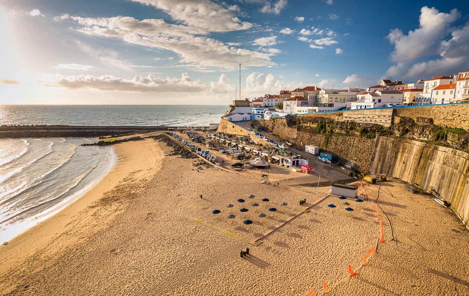Houses on a cliff above a wide beach on a sunny day in Ericeira, Portugal