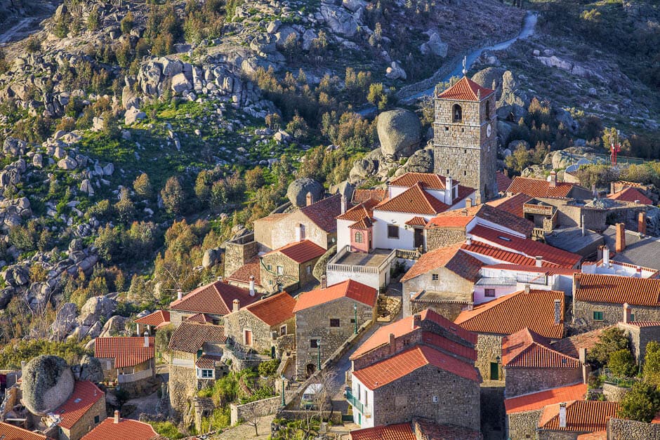 Ancient red roofed houses and a tower surrounded by boulders at the top of a hill in Monsanto, Portugal