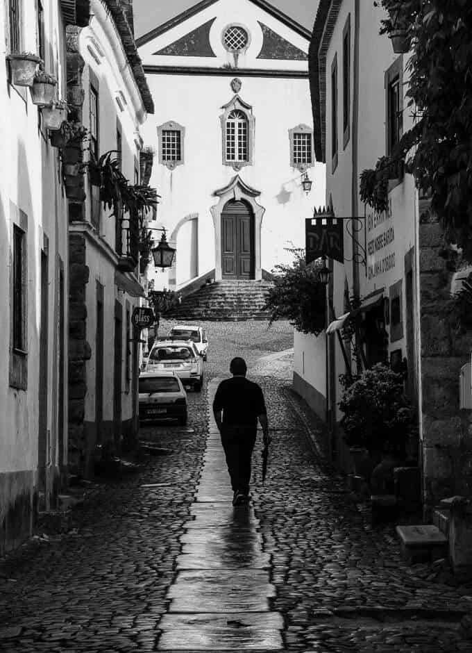 Man walking with umbrella in narrow street in Obidos