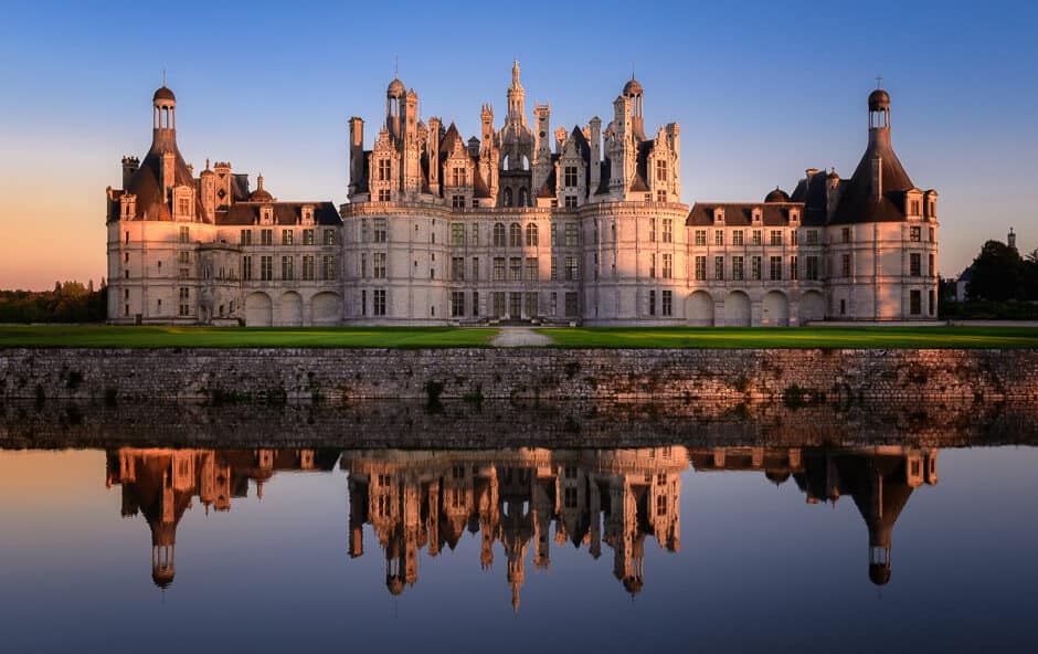A large, majestic castle reflection on water at blue hour