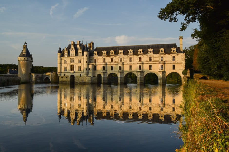 A castle spanning a river, with a reflection, at sunset