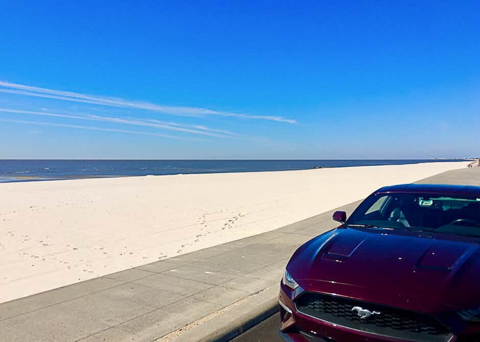 Red car driving along a wide beach