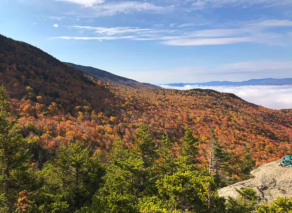 Mountain covered with fall foliage and low clouds in the distance in Vermont, one of the best fall vacations in the U.S.