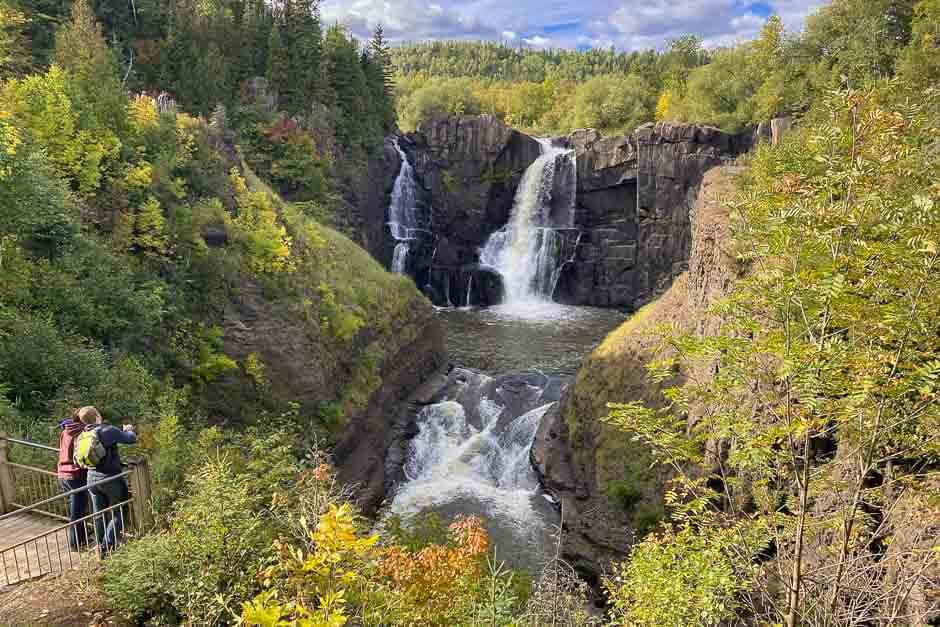 Two people stand at an outlook to view towering waterfalls in Minnesota, a fall U.S. destination.